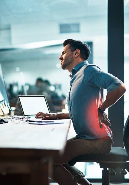 Shot of a young businessman suffering from backache while working at his desk in a modern office